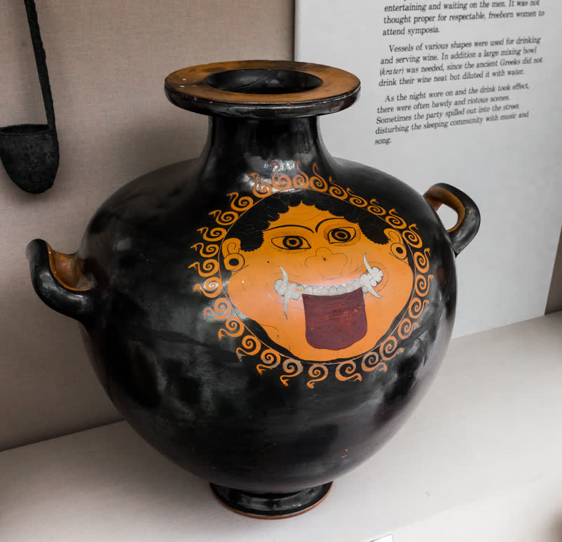 O gorgoneion pintado no bojo do vaso: o rosto redondo de boca escancarada, língua de fora e presas cruzadas, dentro de uma coroa de caracóis que terminam em cabeças de serpente. Hídria (kalpis) ática de figuras vermelhas, ca. 490 a.C., achada em Tarquínia. Museu Britânico, Londres (1867,0508.1048).